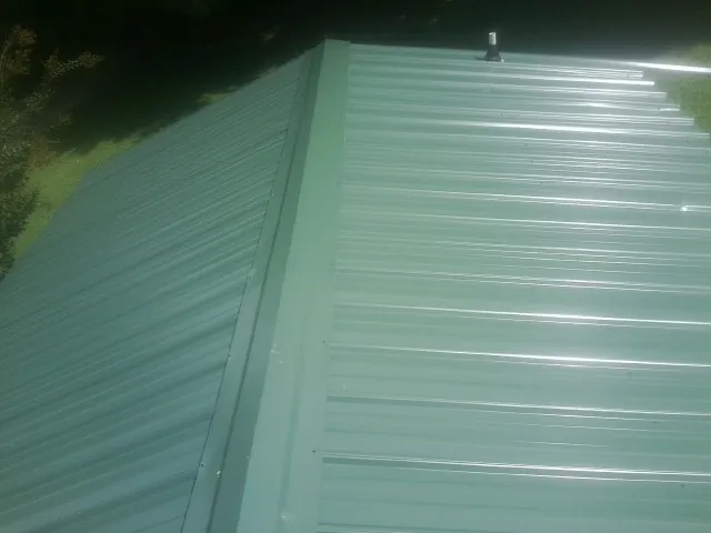 New green metal panels meeting at the ridge of a roof — Flat Roof Repair work by our crew in Morrisville